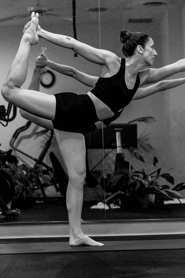 Yoga practitioner in standing bow pose, reflected in the studio mirror